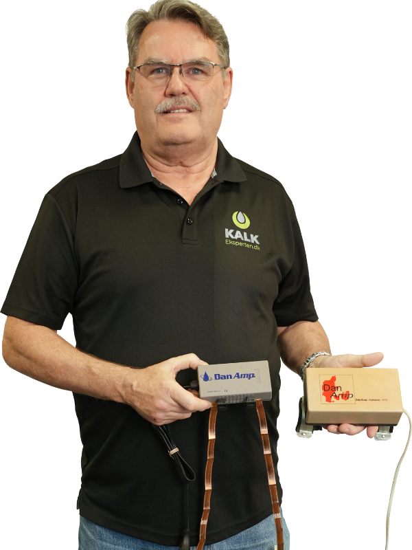 Karsten fra Kalk Eksperten holder en gammel Dan Amp kalkspalter-enhed og en nyere prototype med kobberbånd – illustrerer virksomhedens historie og udvikling i kampen mod kalk
